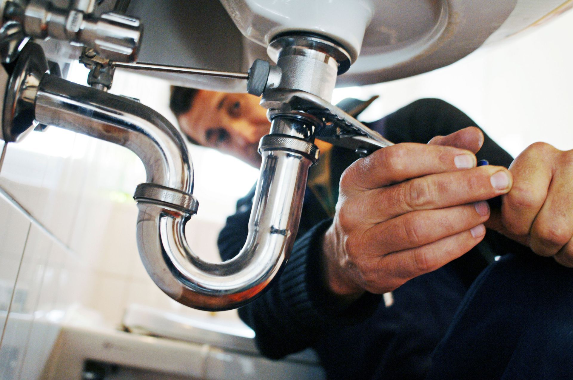 Close-up of an emergency plumber repairing a sink with a tool in a bathroom.