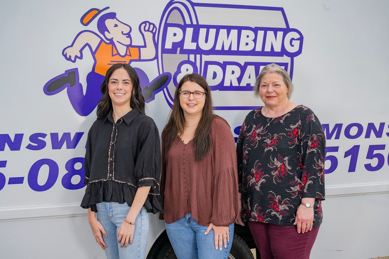 Three women standing in front of a plumbing and drain service truck with logo.