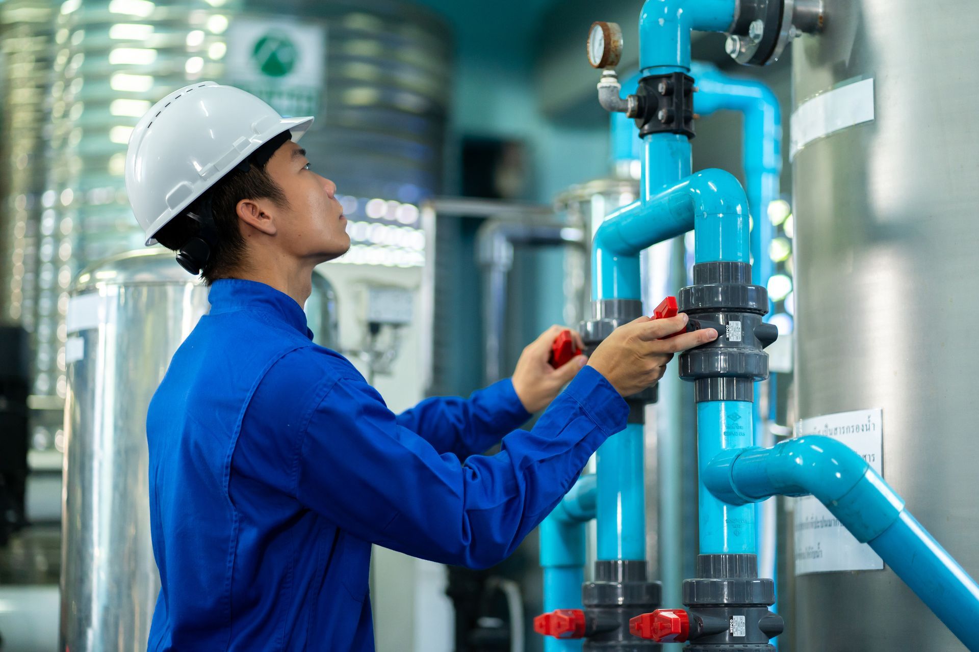 A plumber, wearing a blue shirt and hard hat, is providing 24/7 plumbing services at a plant.