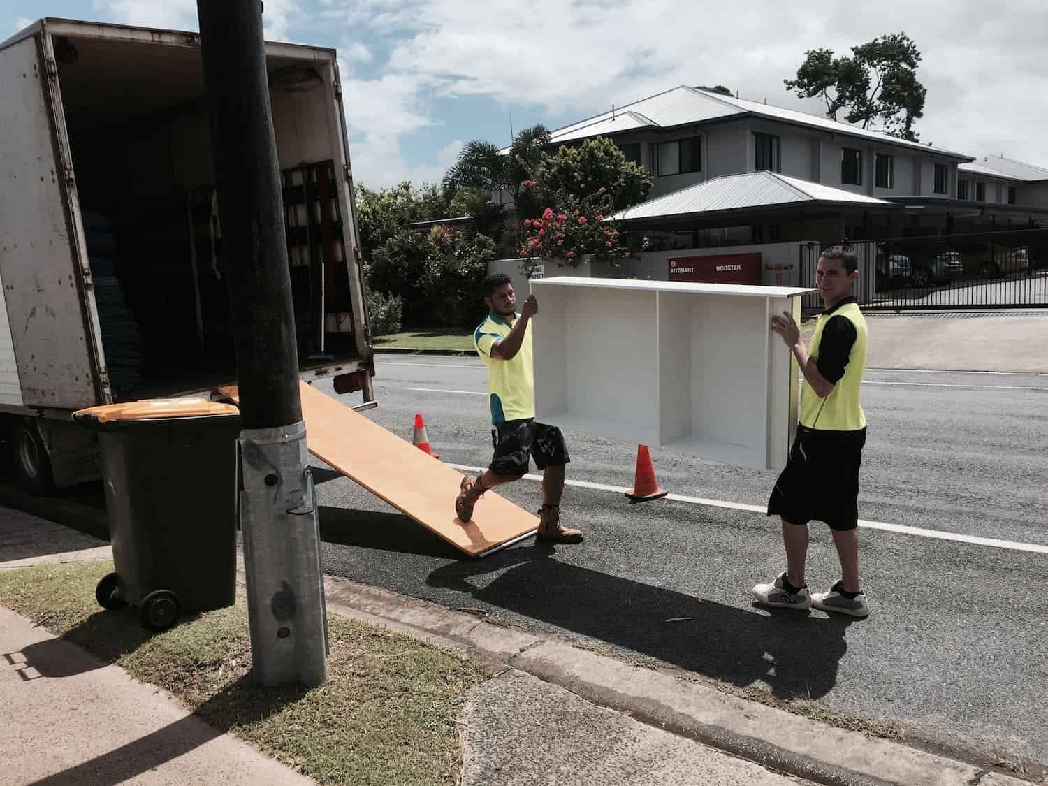 Two Movers Carry a White Cabinet From a Truck — Cairns Mini Movers In Mount Sheridan, QLD
