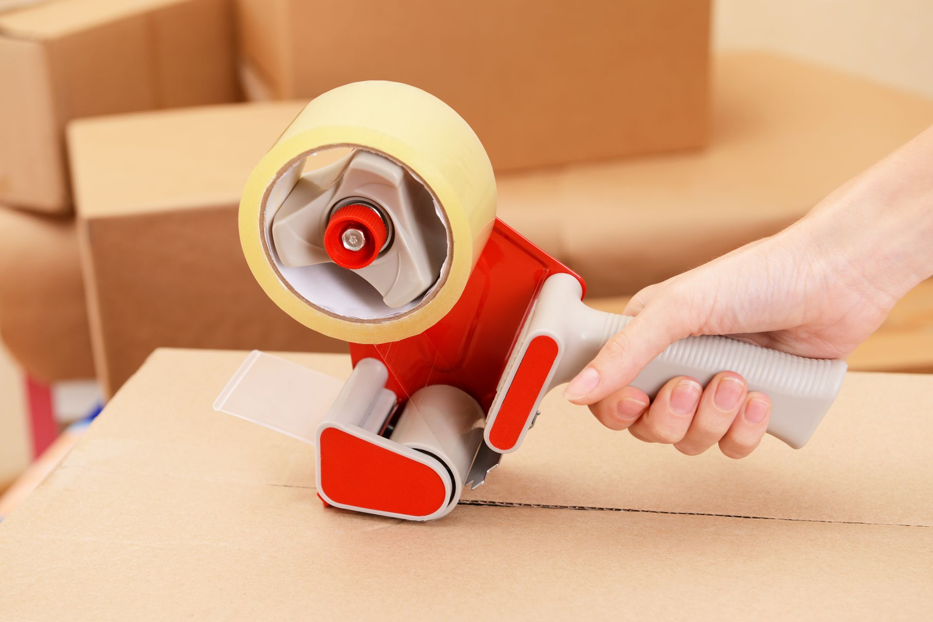 Hand Using a Tape Gun to Seal a Cardboard Box — Cairns Mini Movers In Mount Sheridan, QLD