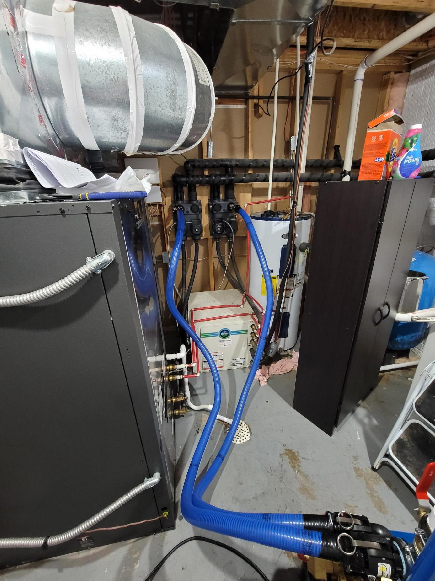 Basement utility area with HVAC ducts, pipes, blue hoses, and a furnace beside storage cabinets.