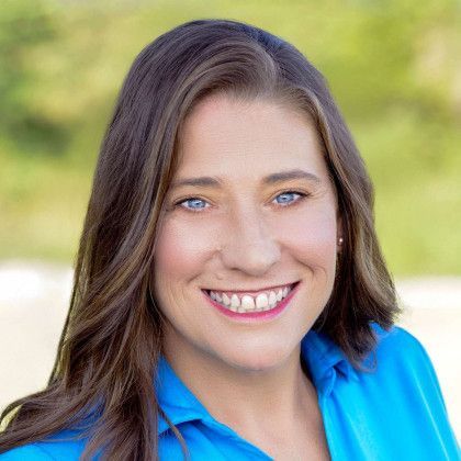 Smiling woman in a blue shirt outdoors with a blurred green background