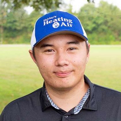 Person wearing a blue cap and dark polo shirt, standing outdoors on a grassy field.