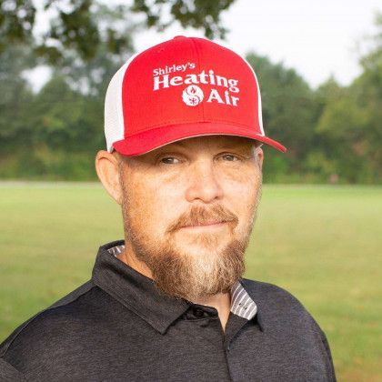 Man in red-and-white cap and black polo standing outdoors in a grassy field