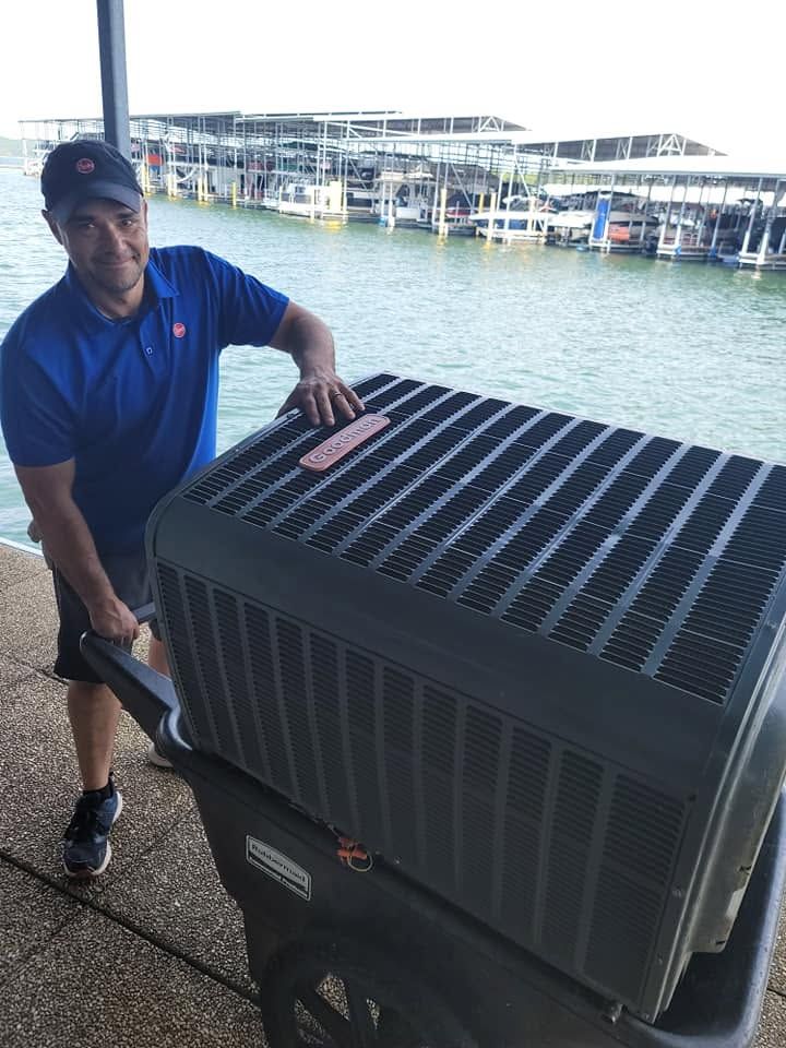 Person in a blue shirt and cap pushing a large black cart by a waterfront pier.