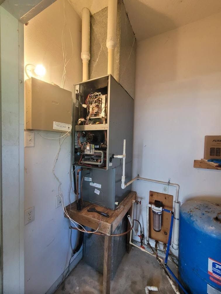 Open furnace with exposed wiring and pipes in a small utility room