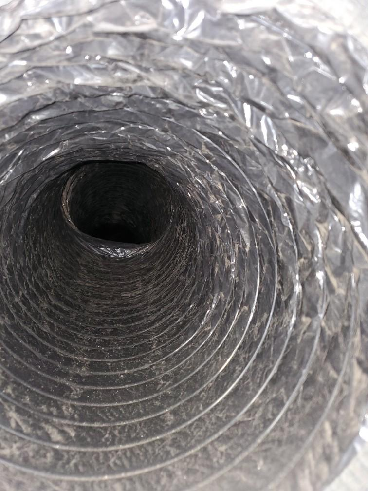 Inside of a flexible metal ventilation duct, showing the spiral ridges and dark opening.