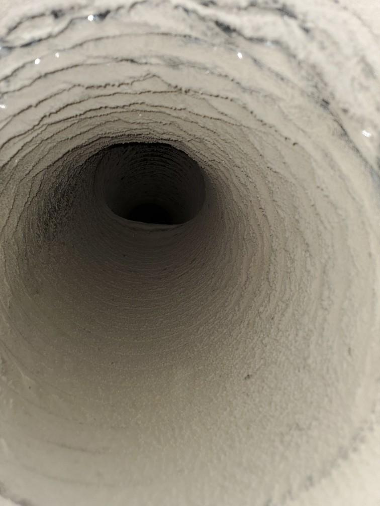 Close-up view down a white cylindrical pipe or tunnel with a dark opening in the center