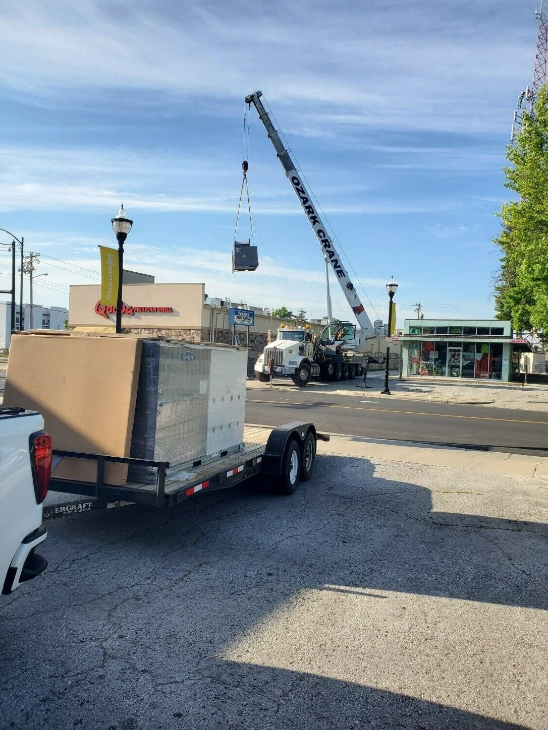 Construction crane lifting a large wrapped crate in a parking lot under a clear blue sky