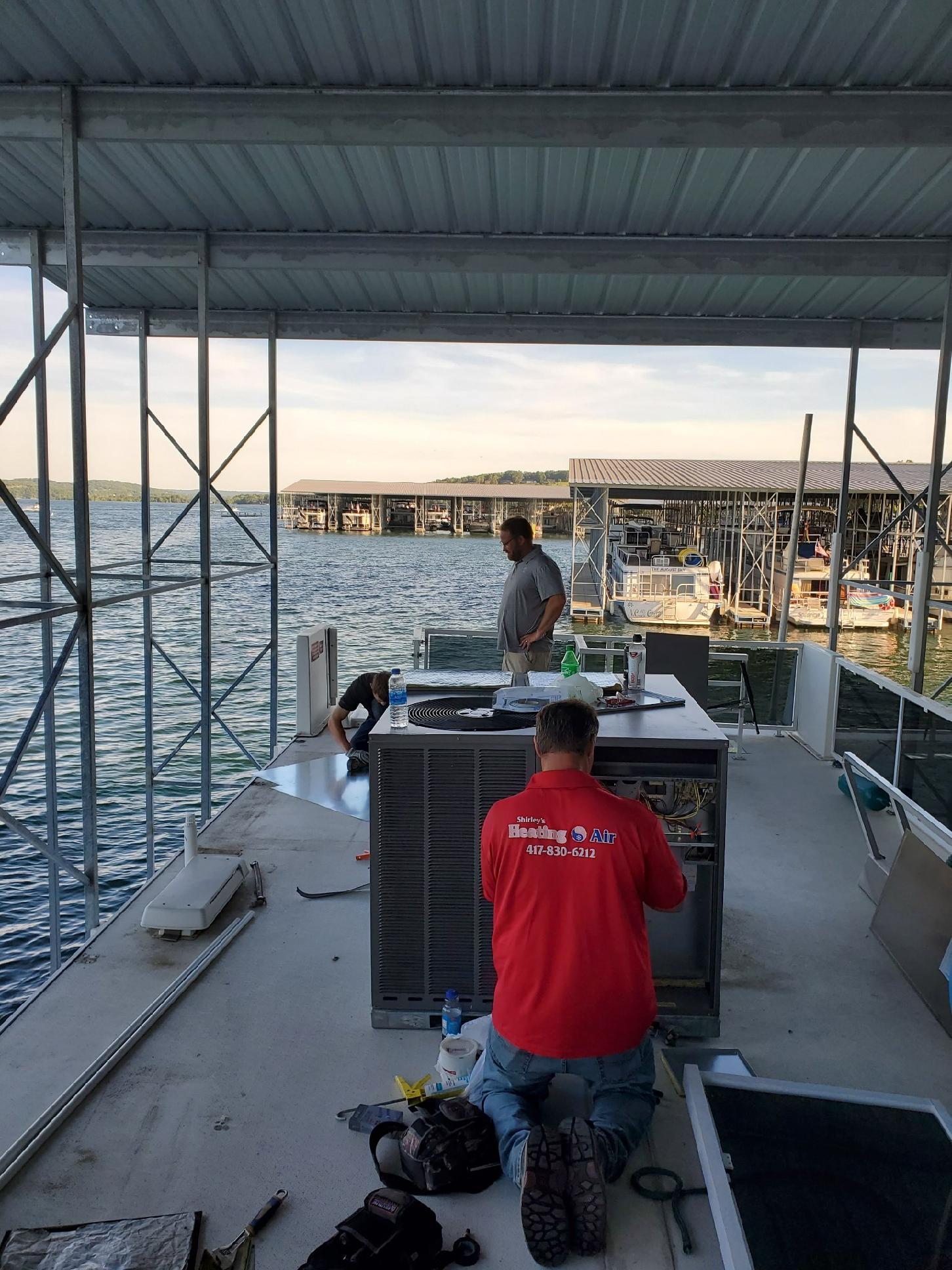 Workers on a dock under a metal roof, handling equipment near the water at sunset.