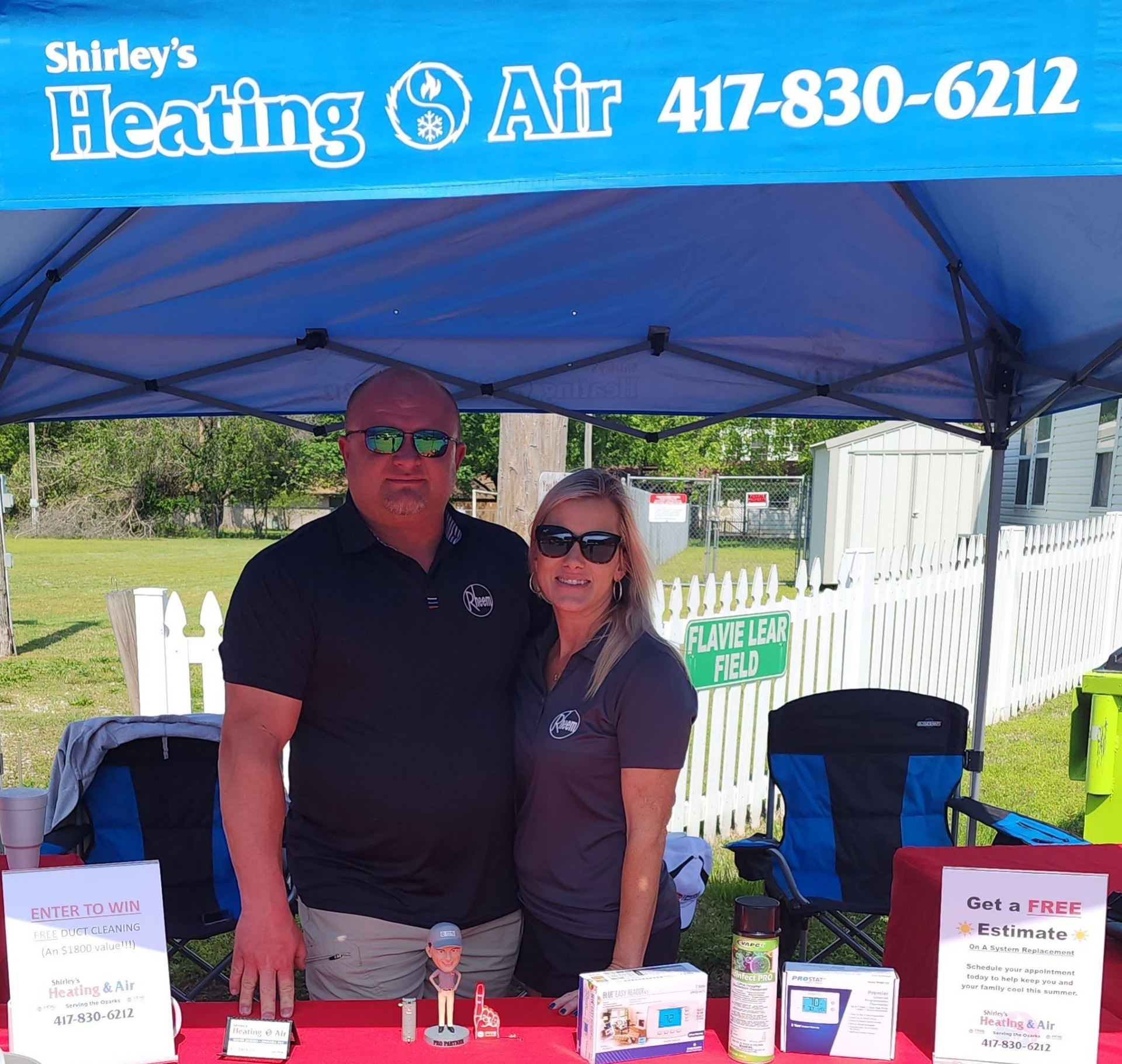 Two people at Shirley’s Heating & Air booth under a blue tent, with flyers and promotional items on the table.