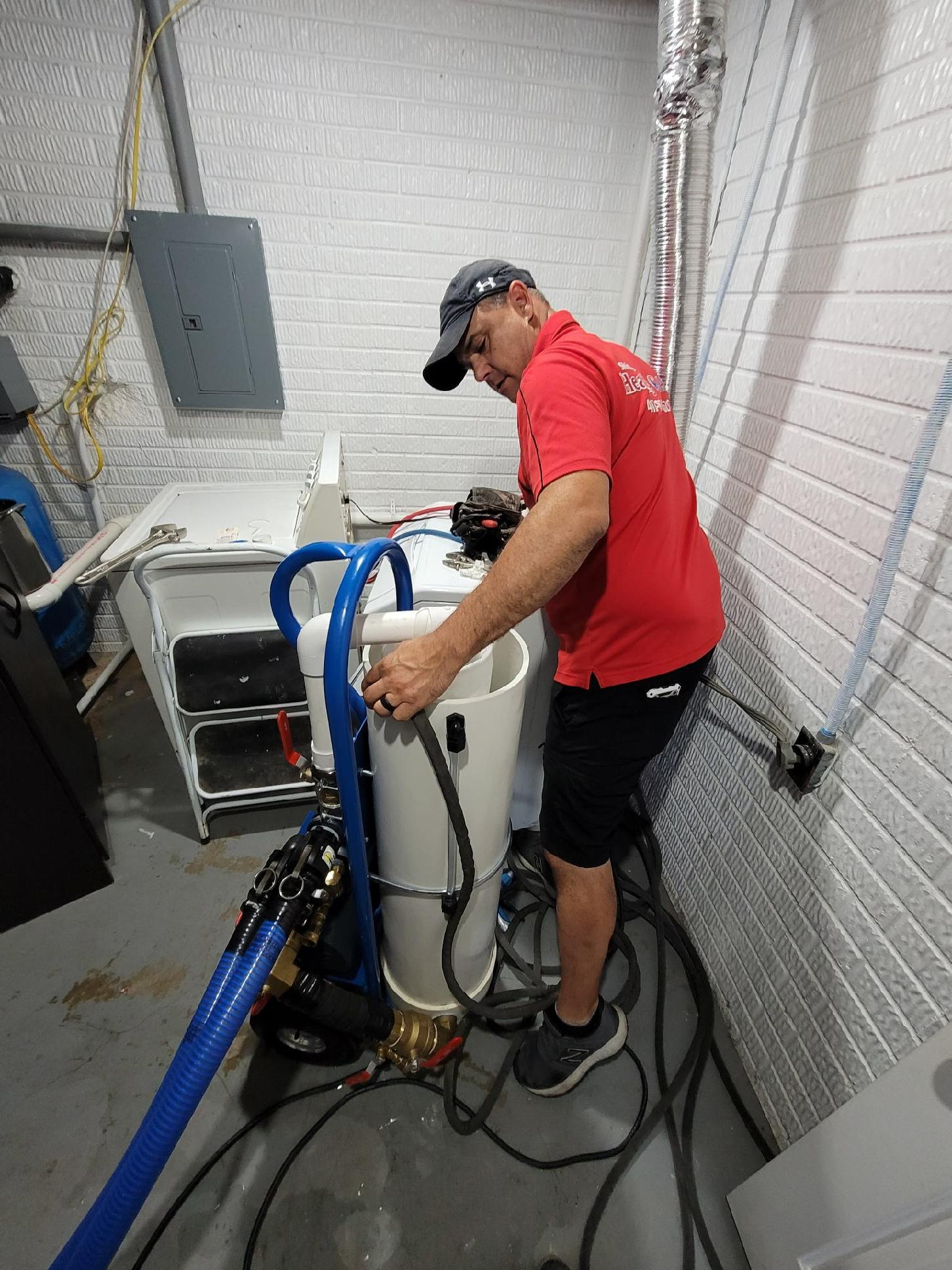 Technician in red shirt servicing a white water treatment unit in a utility room.
