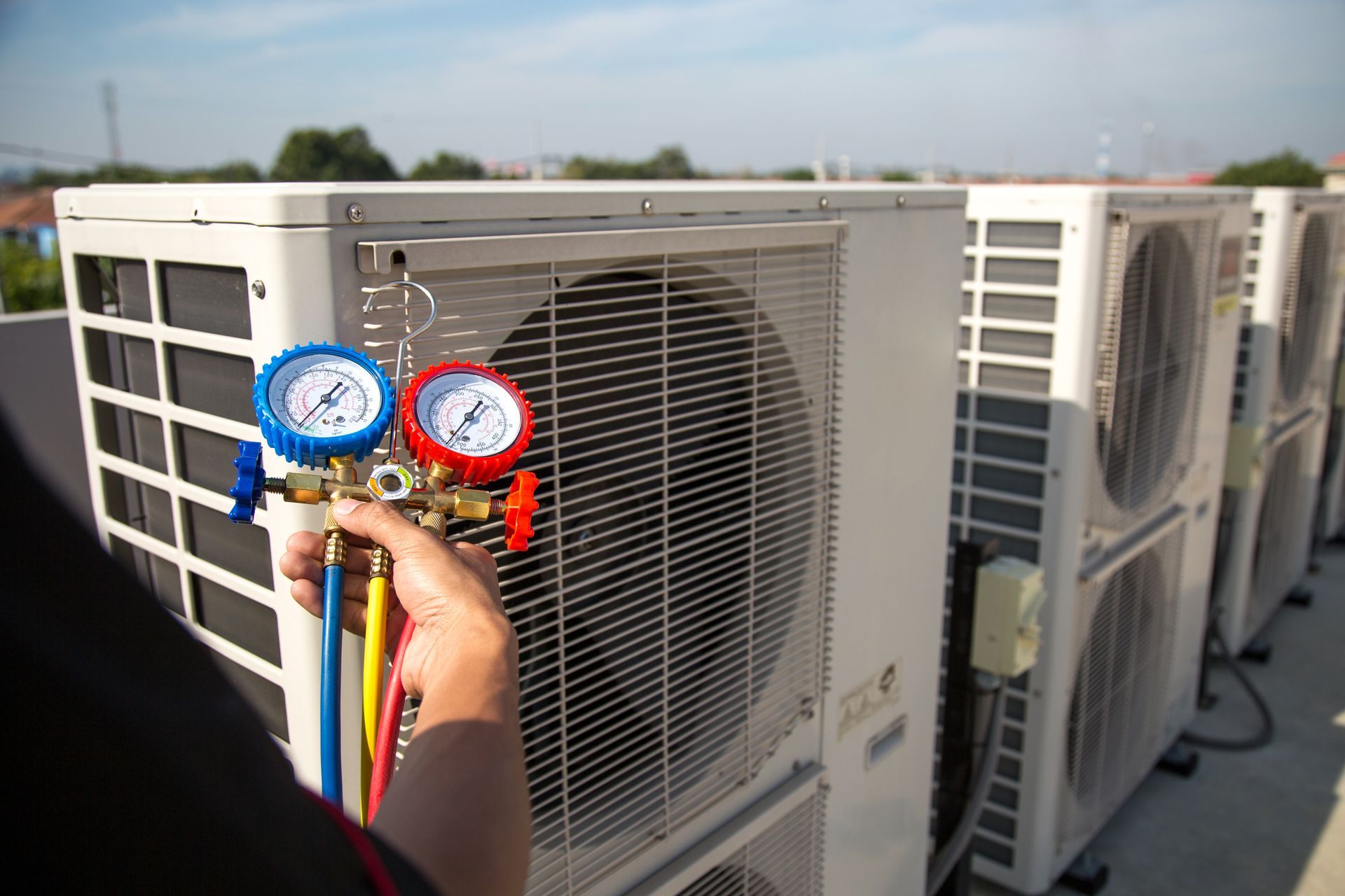 Technician testing rooftop air conditioning units with blue and red gauges attached to a compressor
