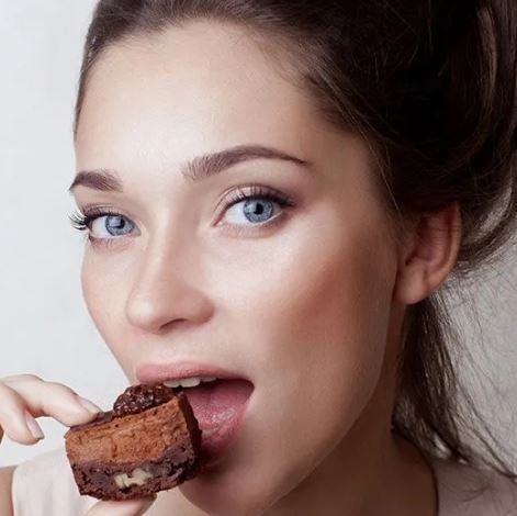Una donna mangia un pezzo di torta al cioccolato con la lingua fuori.