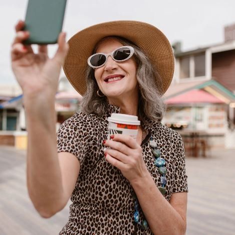 Una donna che indossa un cappello e occhiali da sole si scatta un selfie con il suo telefono.