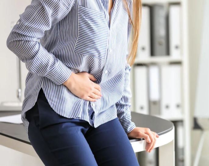 Una donna è seduta alla scrivania con le mani sullo stomaco.