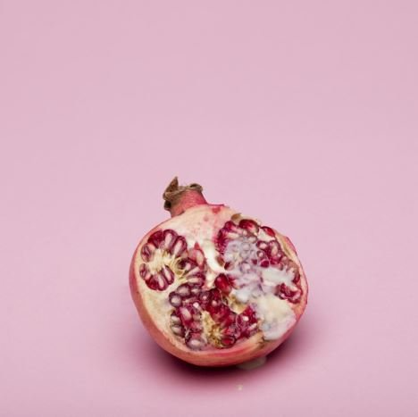 Un melograno è tagliato a metà su uno sfondo rosa.