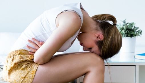 Una donna è seduta sul pavimento e si tiene lo stomaco in preda al dolore.