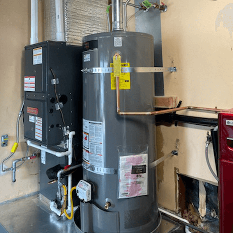Furnace and water heater in a utility room. Gray appliances, white pipes, and yellow gas lines against tan walls.
