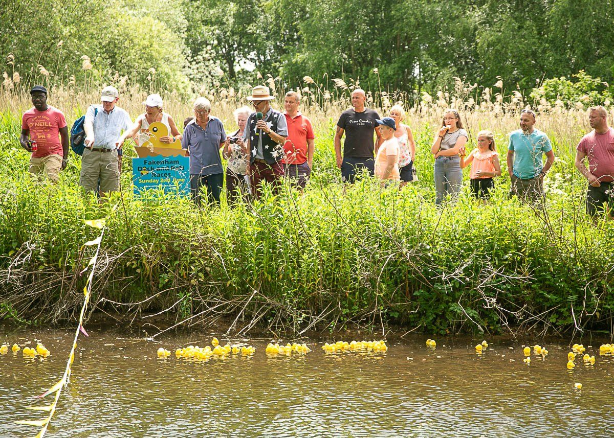 Group of people watching small ducks floating by in Fakenham Duck Race