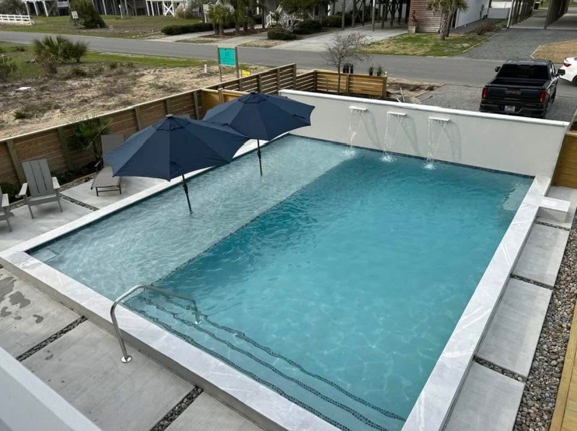 Rectangular outdoor swimming pool with two blue umbrellas and a white wall surround