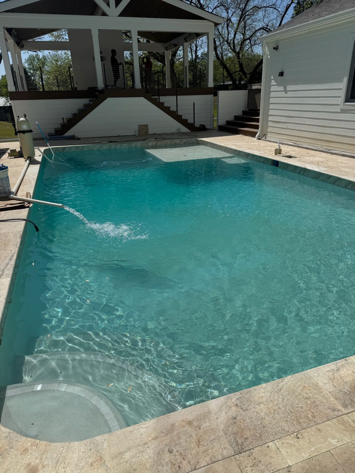 Backyard swimming pool with turquoise water, gazebo, and a white house beside it.