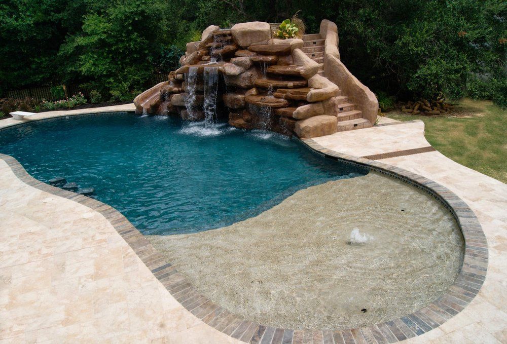 A large swimming pool with a waterfall and slide by Caroline Pool Plastering in Charlotte, NC