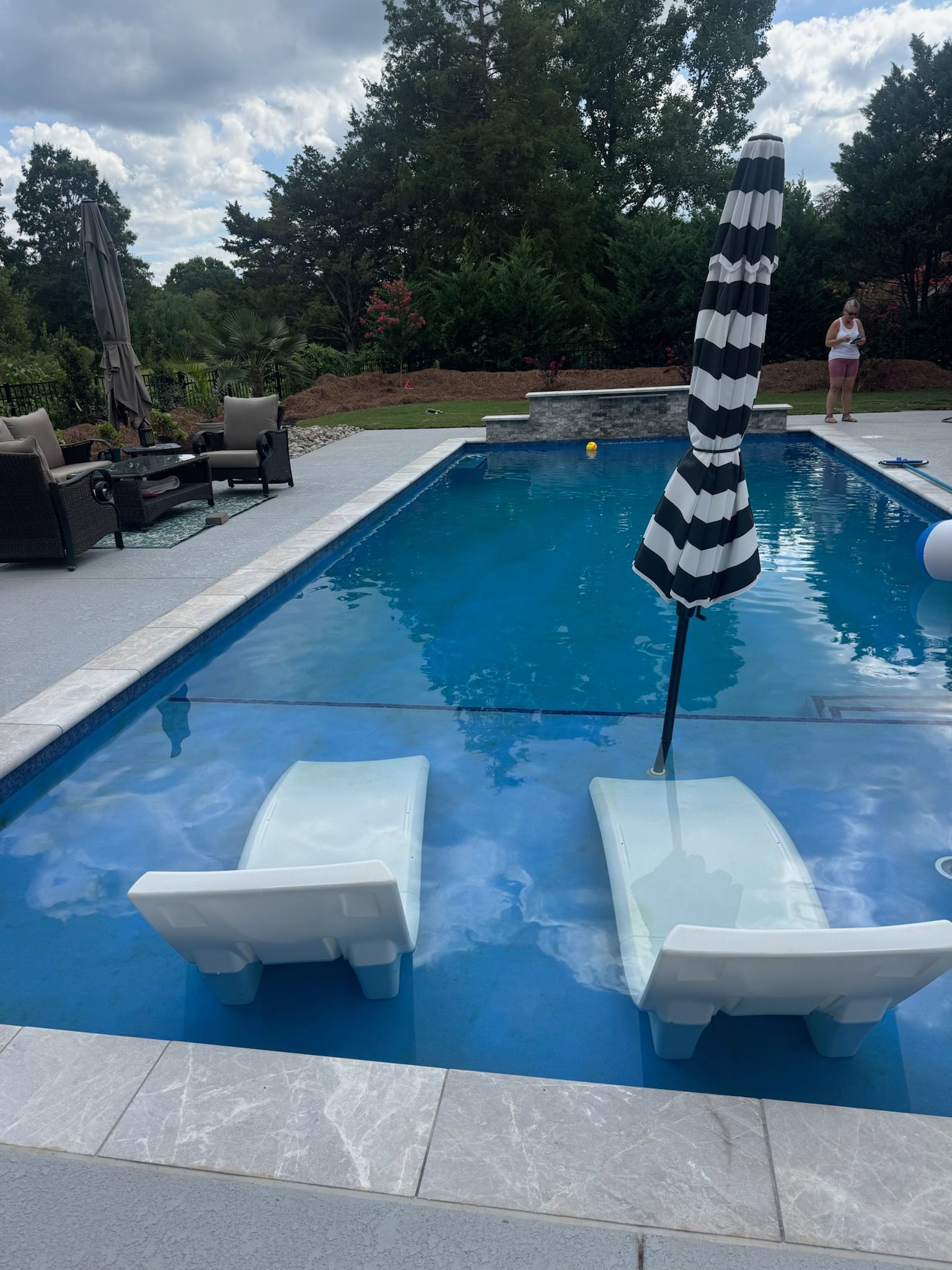 Poolside lounge chairs facing a blue swimming pool with a black-and-white striped umbrella