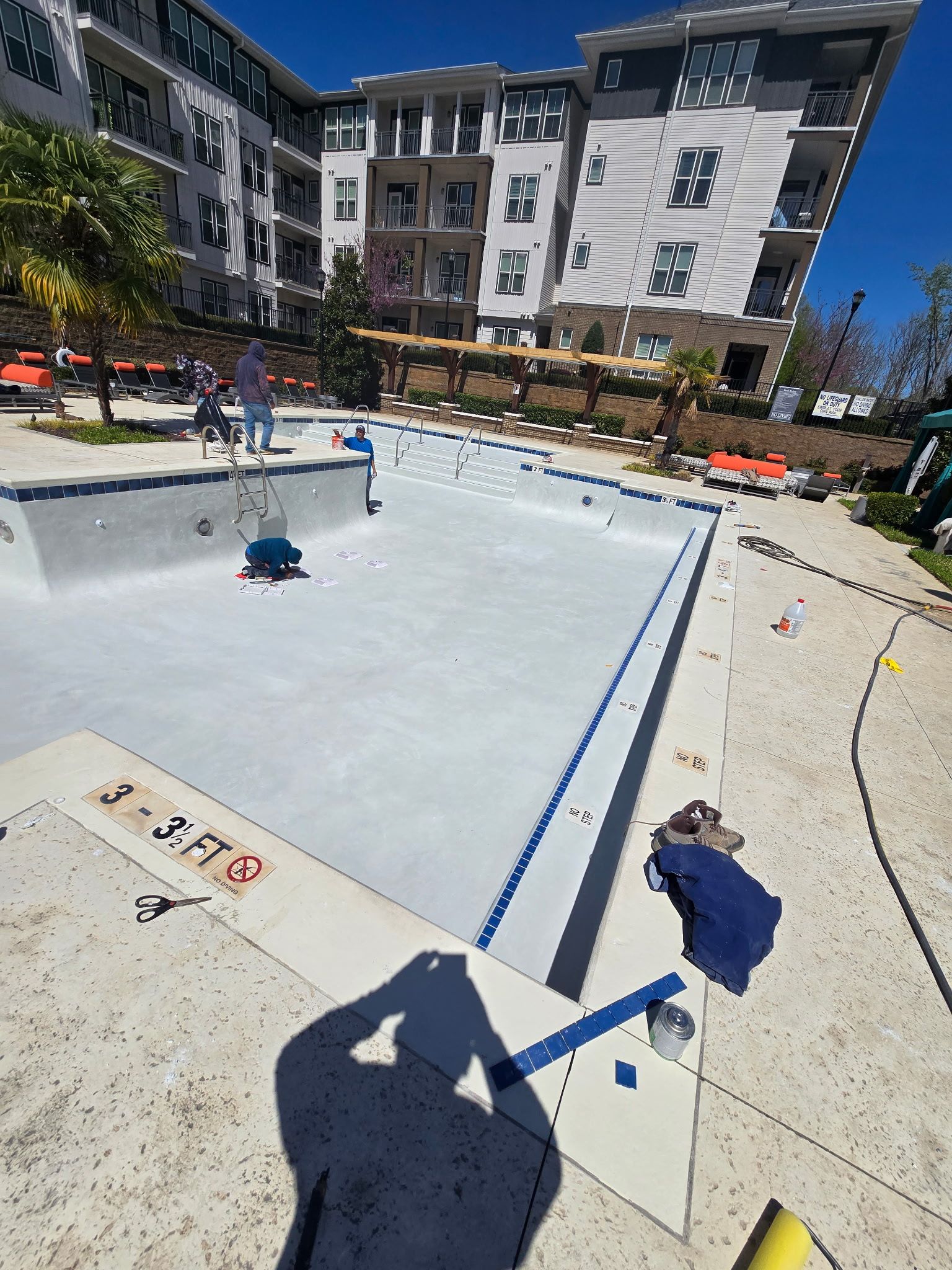 Empty outdoor ice rink at a modern apartment complex, with blue barriers and people in the background.