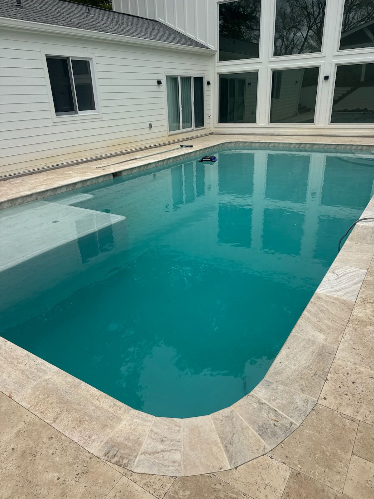 Rectangular backyard pool with turquoise water beside a white house and stone patio.