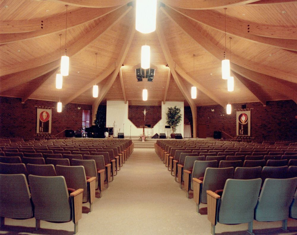 Interior of a church auditorium with rows of seats facing a raised stage with a cross and a plant.
