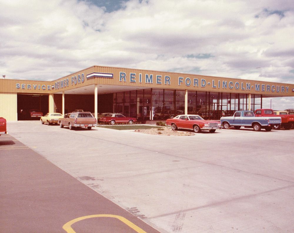 Ford dealership with multiple cars on display. Sign reads: Reimer Ford-Lincoln-Mercury.