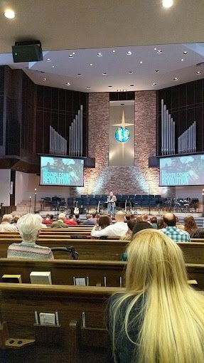 Church service in progress; a person is speaking on stage; congregants in pews.