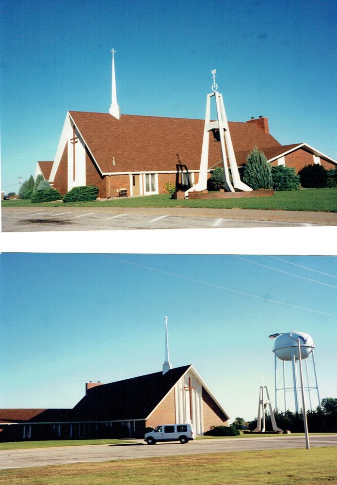 Church building with tall steeple and bell tower on a clear day; a water tower is also present.