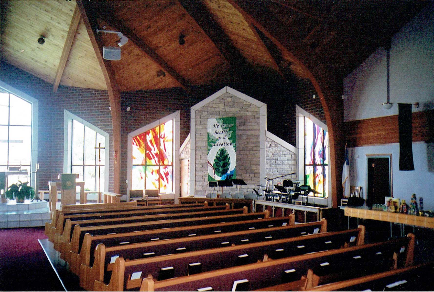 Interior view of a church sanctuary with wooden pews, stained glass, and a stone altar.