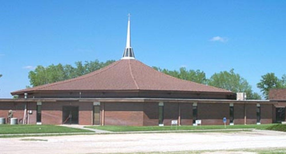 Brown brick church with conical roof and spire, under a blue sky.