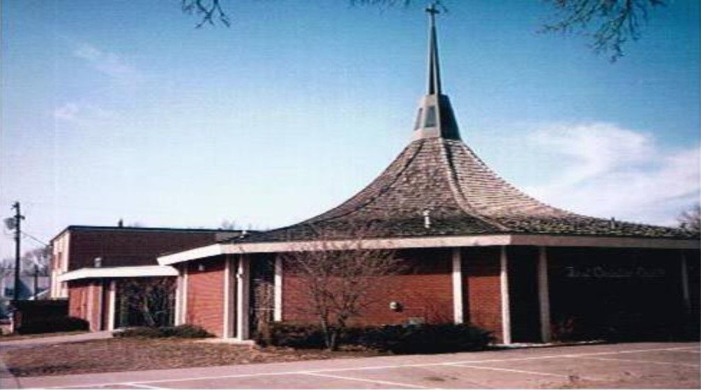 Red brick church with a tall steeple and brown curved roof.