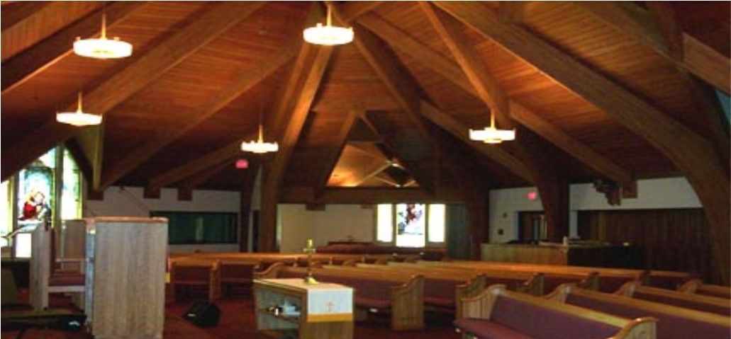 Interior view of a wooden church with a peaked ceiling, rows of pews, and hanging lights.