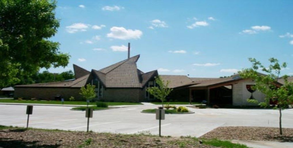 Church building with angled roof, chimney, and trees against a blue sky.