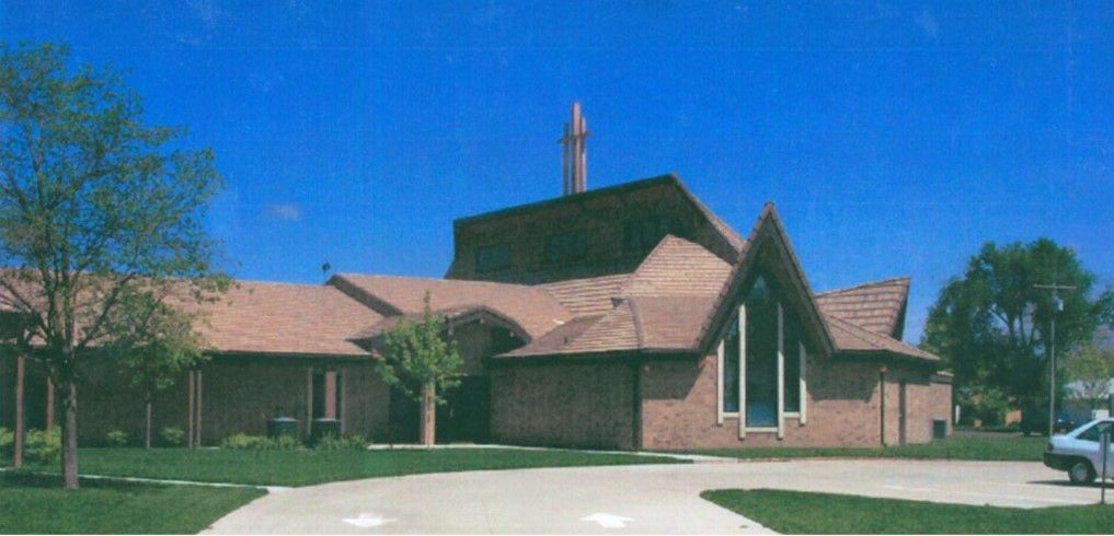 A brick building with a pointed roof and tall spire, set against a bright blue sky.