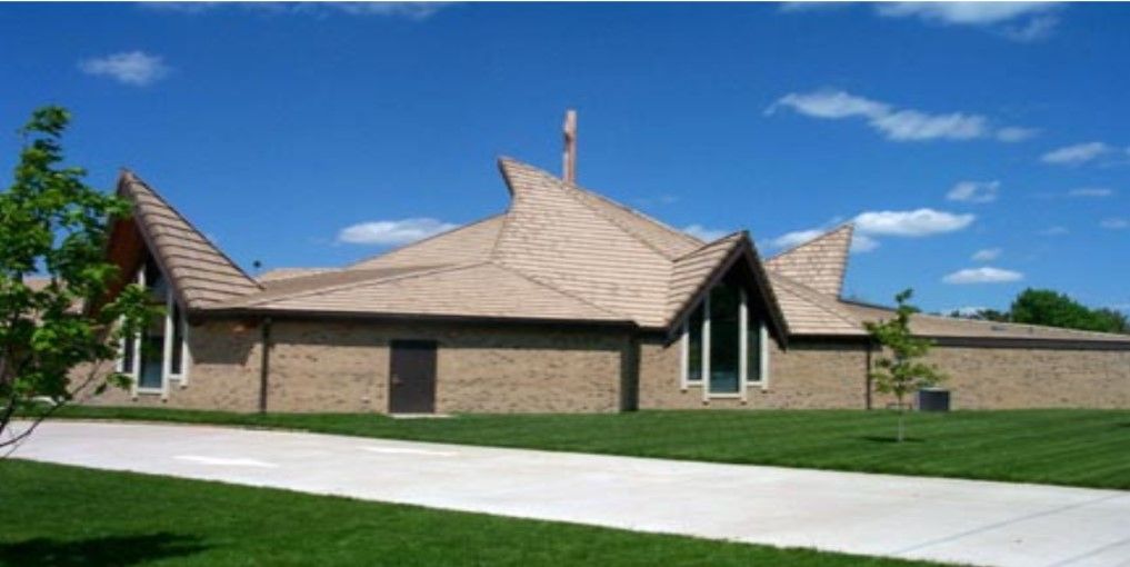A beige brick building with a uniquely shaped roof against a bright blue sky and clouds.