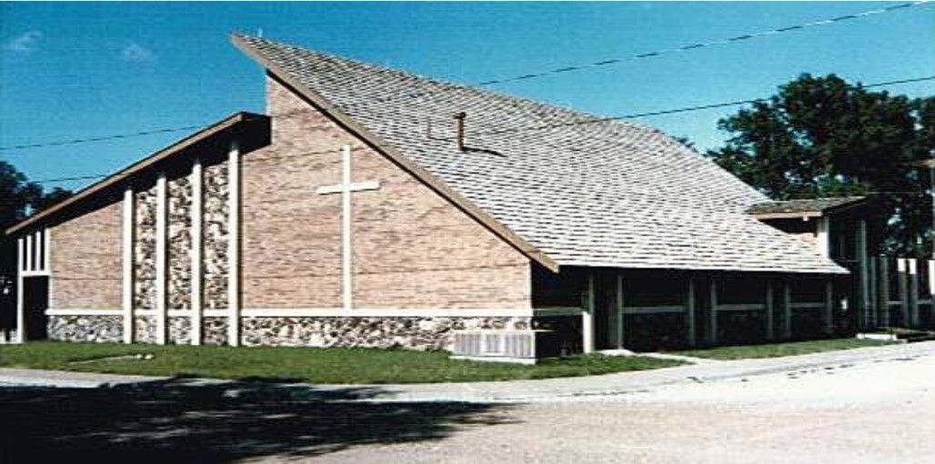 Church building with a white cross on the brick facade and a textured roof.