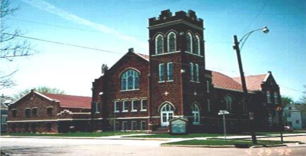 Brick church building with a tower, on a sunny street corner.