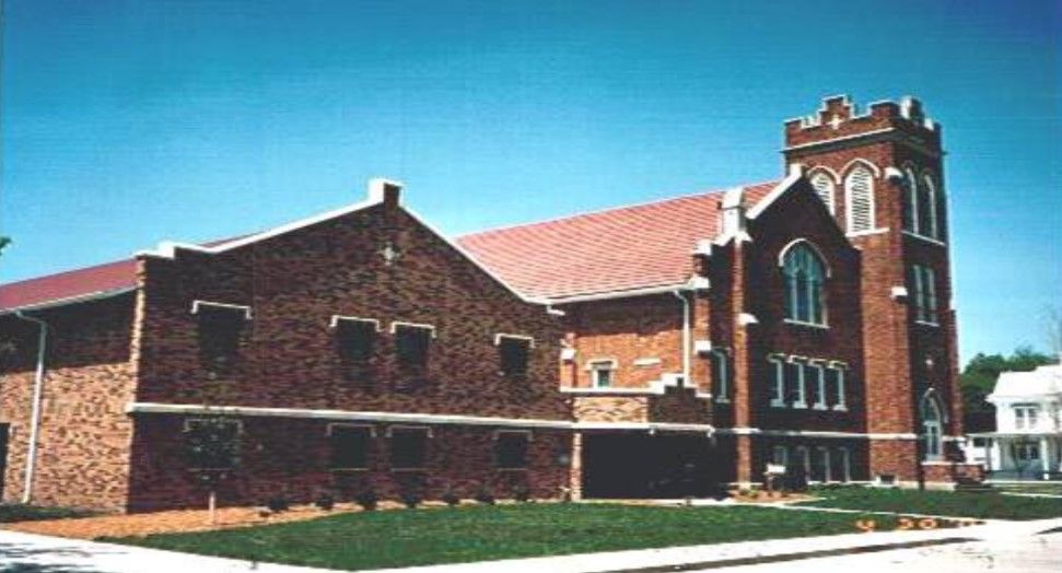 Brick church with a red roof and a tall bell tower under a blue sky.