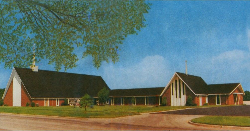Church building with red brick exterior, set against a blue sky, with a tree in the corner.