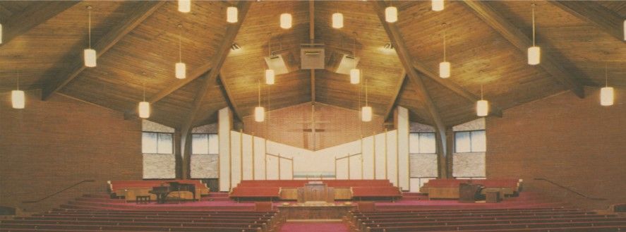 Interior of a church with wooden ceiling, red carpet, and hanging lights.