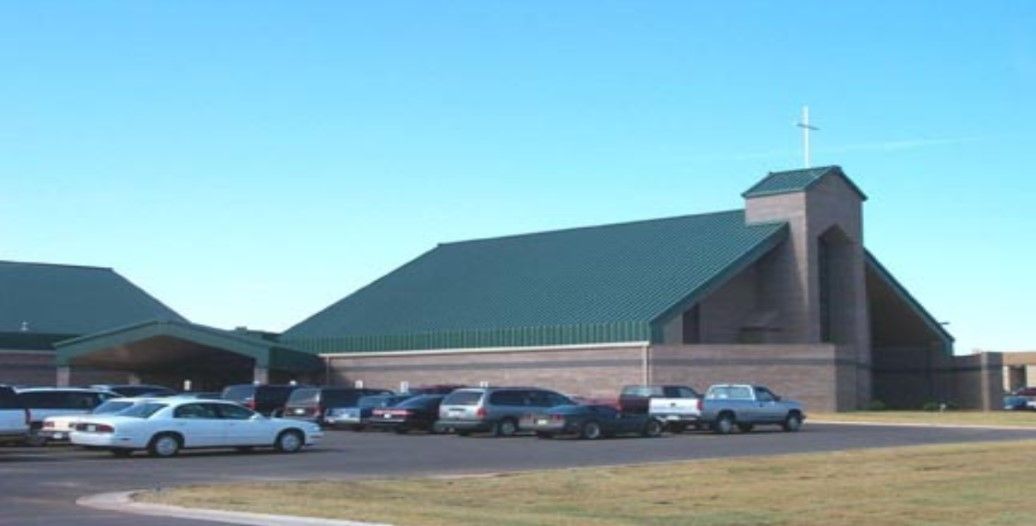 Church building with green roof, cross on top, and parked cars in front.