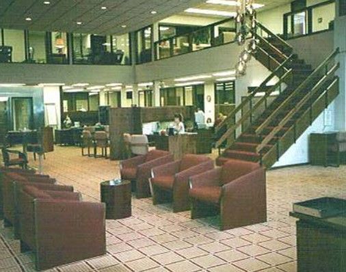 Interior of an office building with a staircase, seating area with red chairs, and a two-story layout.