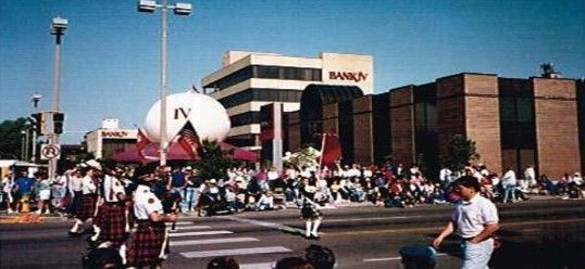 A parade with bagpipers on a crosswalk; large white sphere and spectators fill the street.